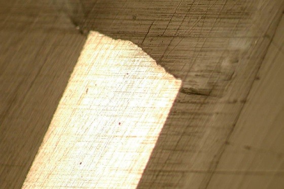 Obr. 15 Metalografický výbrus leptané šablony s ukázkou typického „zobáčku“ ve středu a s mírně kónickým tvarem otvoru pro lepší uvolňování pasty. Síla plechu je 150 μm.